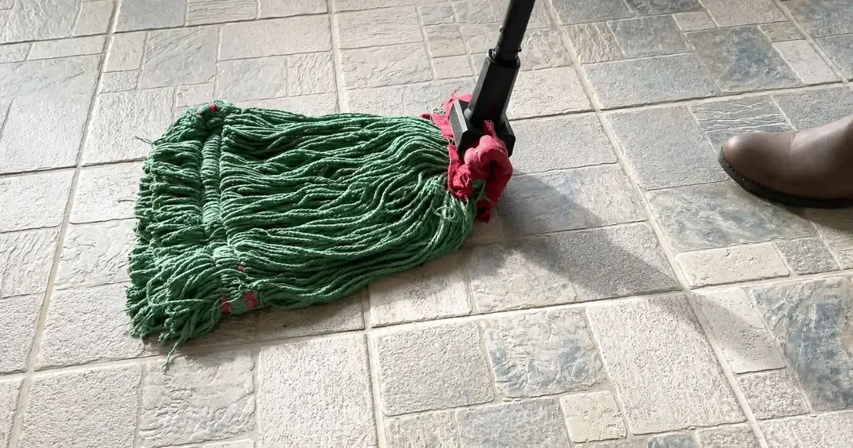 Green wet mop cleaning a textured tile floor.